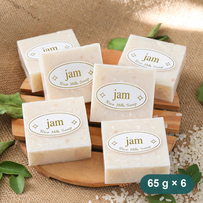 Six rice milk soap bars stacked on a wooden board with rice grains