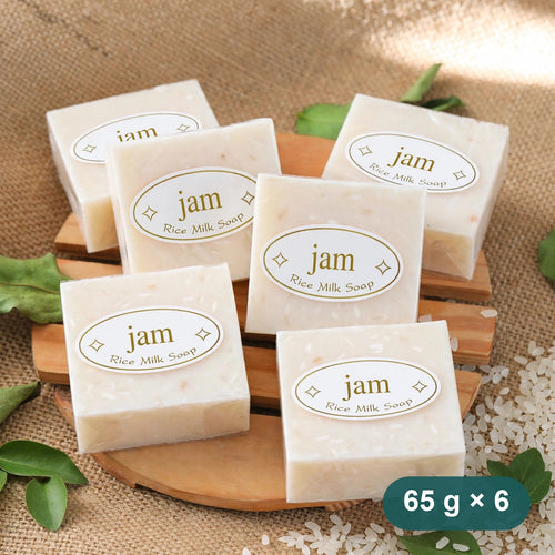 Six rice milk soap bars stacked on a wooden board with rice grains